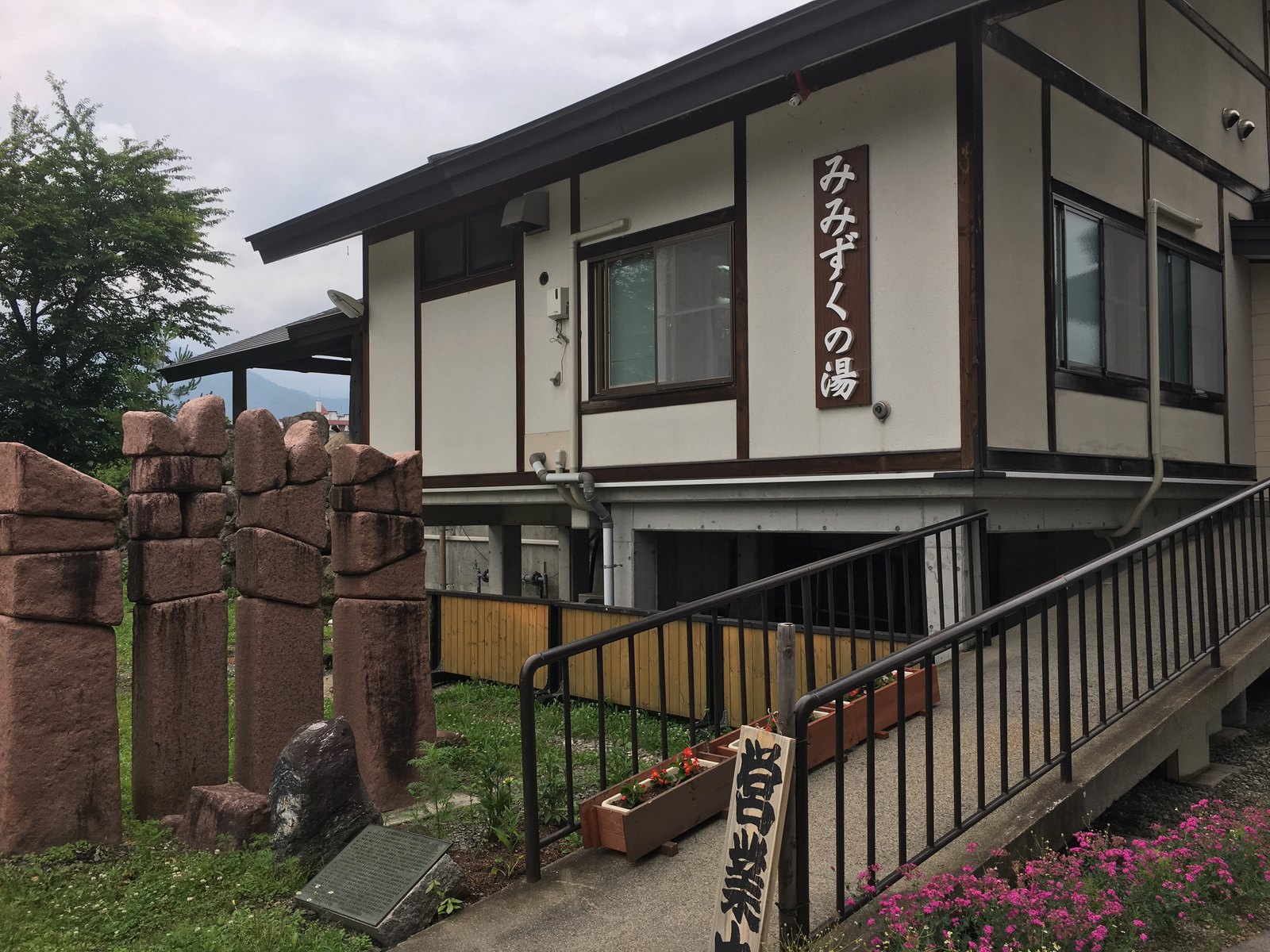 白馬八方温泉みみずくの湯の外観。「みみずくの湯」と書かれた木の看板、入口へ上がるスロープと手すり