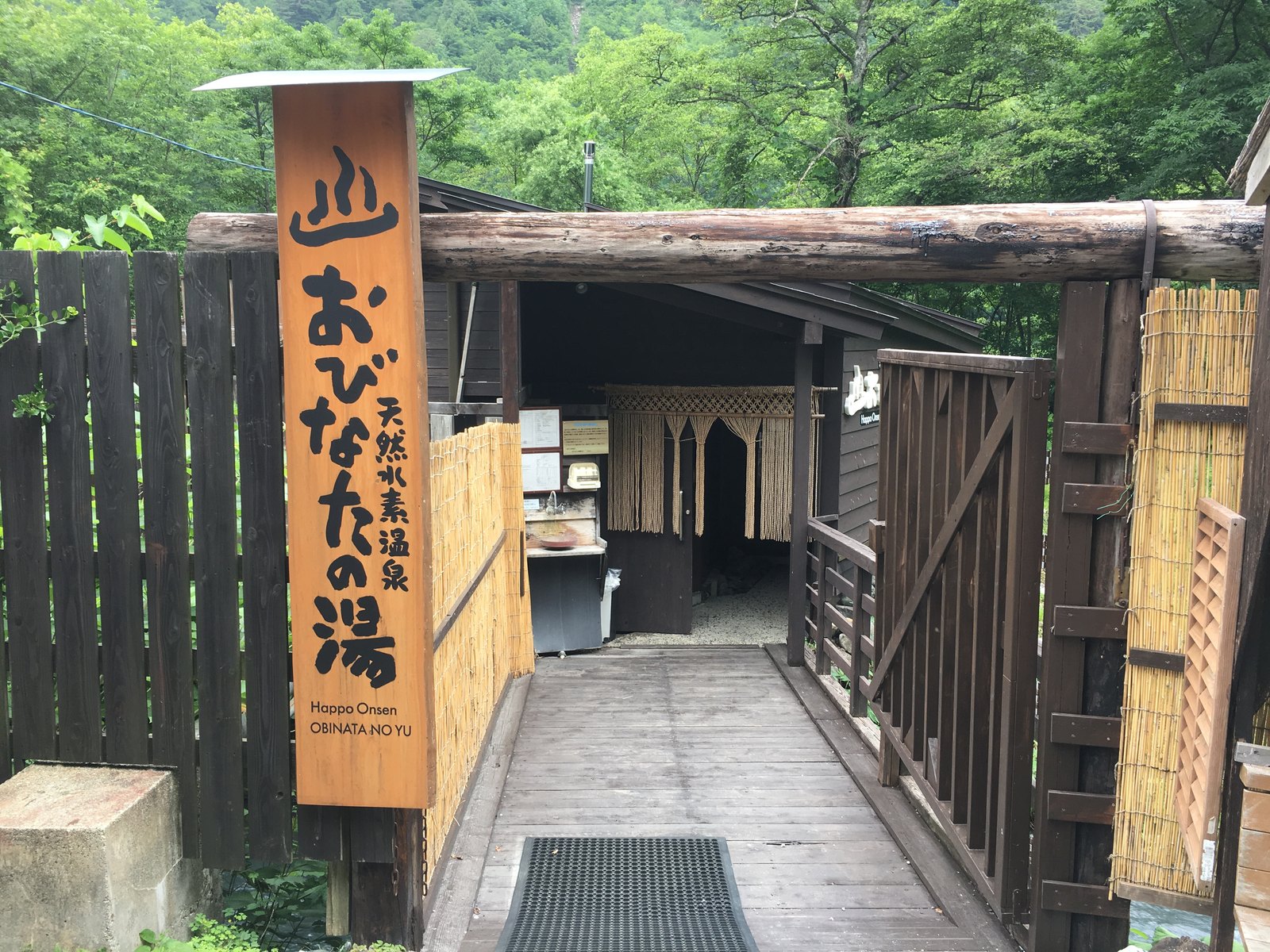 おびなたの湯の入口。「天然水素温泉 おびなたの湯」と書かれた木の看板と、板張りの通路、暖簾のかかった受付